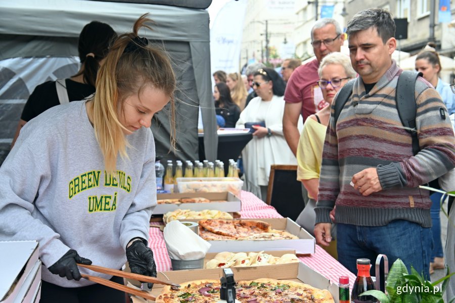 Stoisko z pizzą na festiwalu „Kulinarna Świętojańska”. Na pierwszym planie: młoda kobieta łapie kawałek pizzy. Obok stoiska kolejka uczestników, którzy chcą spróbować wyrobów // fot. Magdalena Czernek