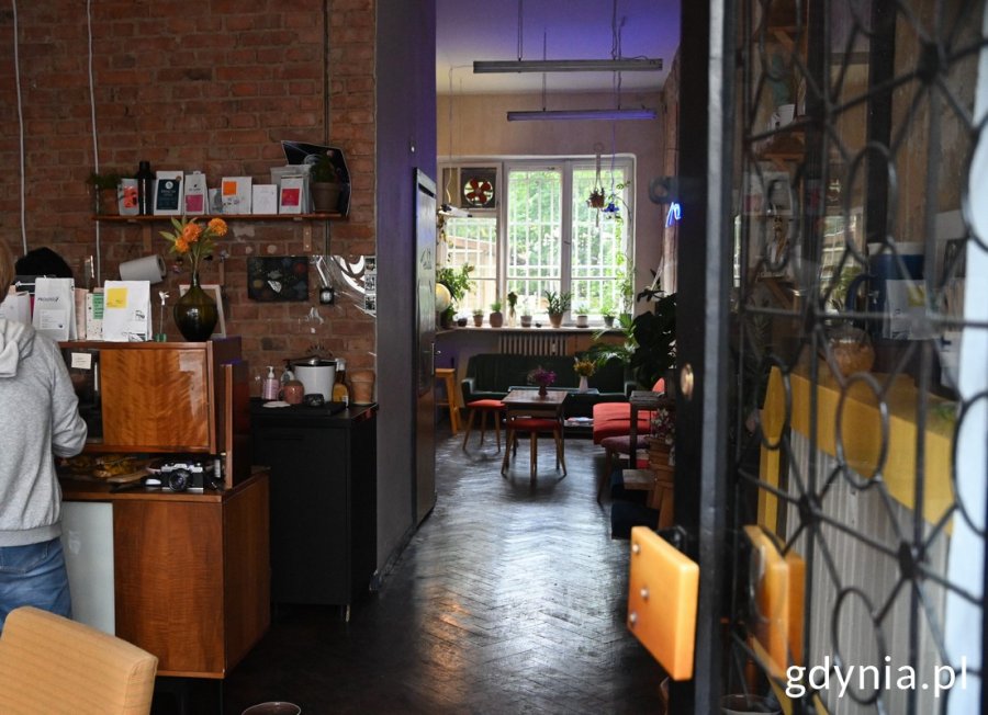 Wnętrze kawiarni „Kosmos”, bar i meble: kanapy, stół oraz kwiaty
