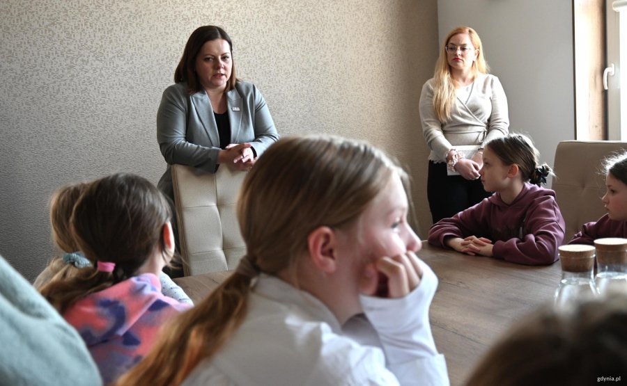 Dzieci za stołem, dwie kobiety stoją obok