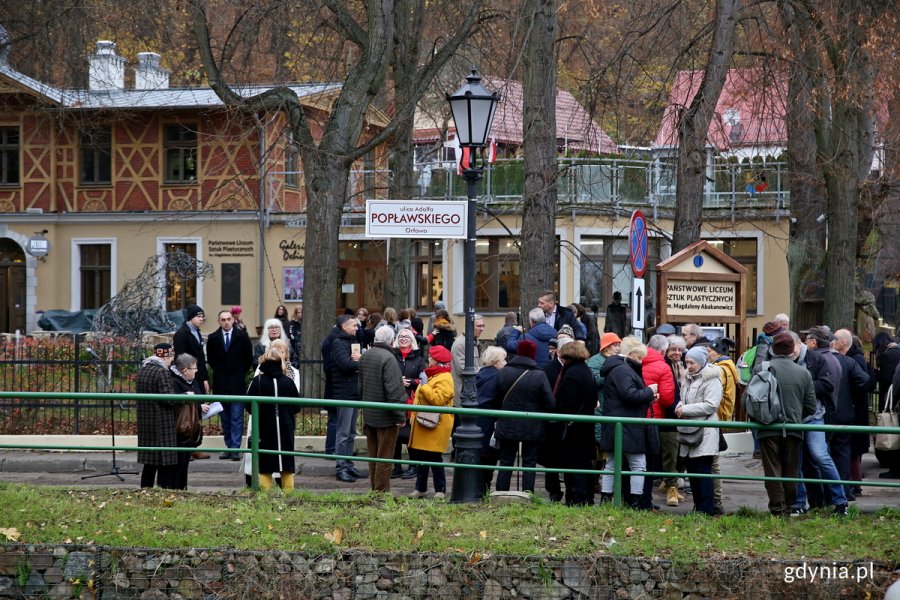 Grupa ludzi stoi pod tablicą z nazwą ulicy.