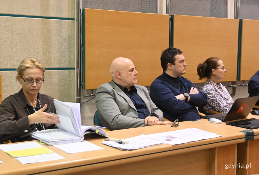 na zdjęciu ludzie przy biurku i kobieta przeglądająca dokumentację