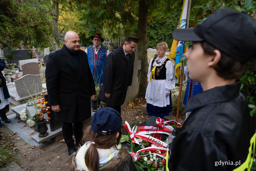 Mężczyzna w czarnym garniturze i kobieta w regionalnym stroju nad grobem.