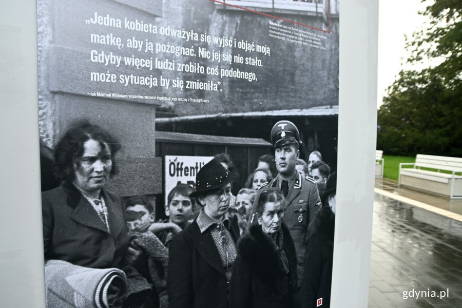 Plansza z bialo-czarnym zdjęciem, na którym widać kobiety i niemieckiego żołnierza. Fragment wystawy „Byli sąsiadami. Ludzkie wybory i zachowania w obliczu Zagłady” na skwerze Kościuszki // fot. Magdalena Czernek