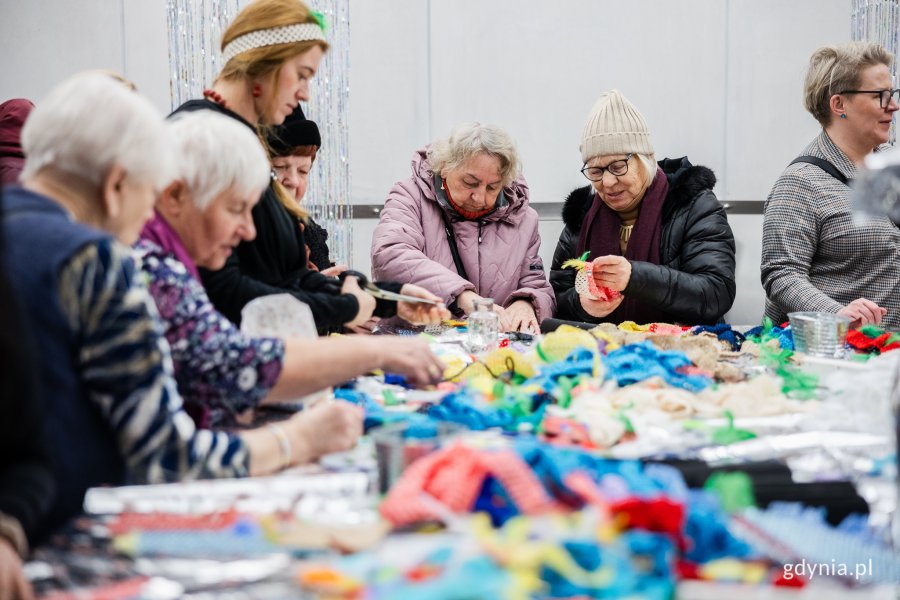 Uczestnicy warsztatów kreatywnych w klimacie lat 70. i 80. zorganizowanych z okazji 98. urodzin Gdyni w Polsat Plus Arenie Gdynia stoją przy stole z kolorowymi opaskami, piórami i innymi akcesoriami 