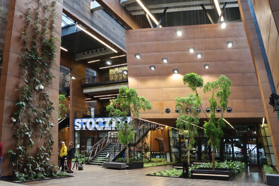 Hol Europejskiego Centrum Solidarności, nowoczesne wnętrze budynku wypełnione roślinami i 2 osoby oczekujące na spotkanie