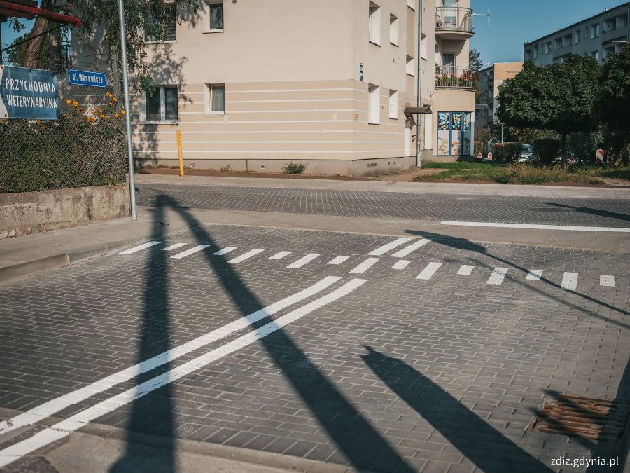 chodniki, wyniesione skrzyżowanie z kostki oraz przejścia dla pieszych po przebudowie. Widoczne oznakowanie, w tle budynki i tereny zielone