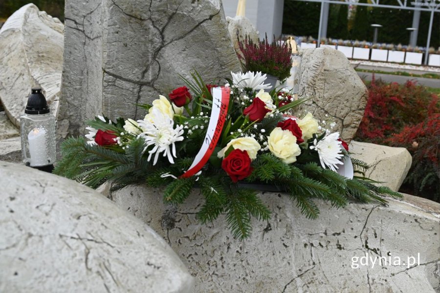 Białe i czerwone kwiaty z zielonymi liśćmi na pomniku z szarych kamieni
