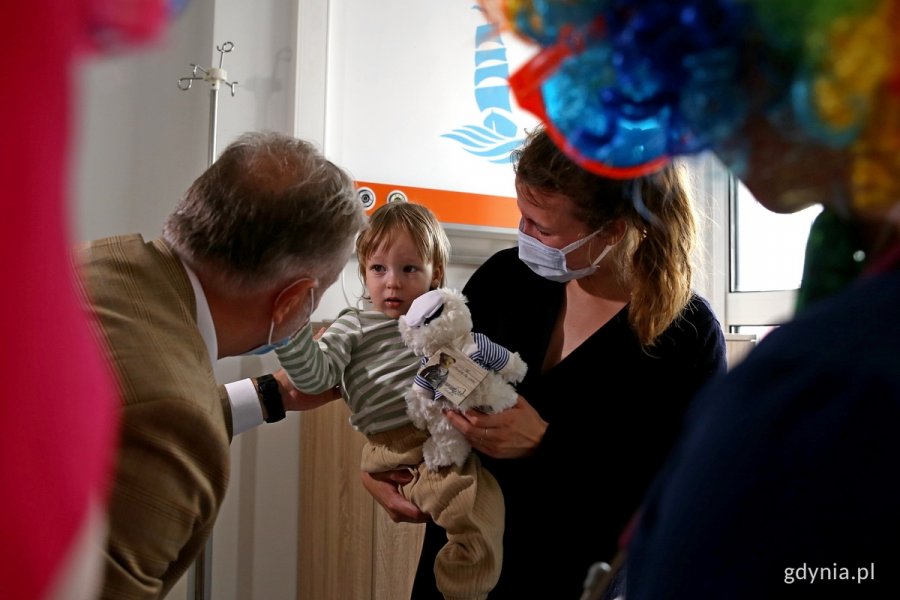 W pokoju szpitalnym stoi prezydent Gdyni i wita się z małym chłopcem na rękach mamy.