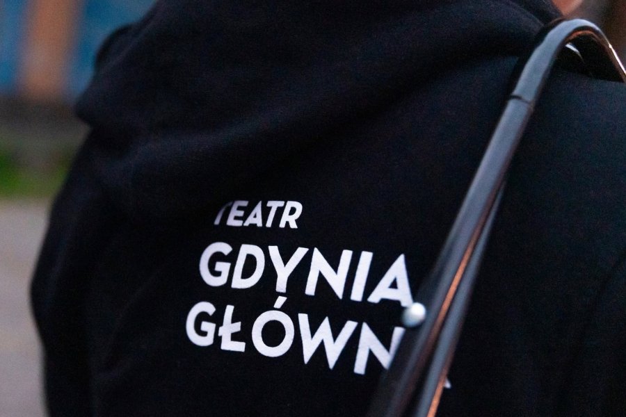 Osoba w bluzie Teatru Gdynia Gł&oacute;wna podczas pokazu spektaklu &bdquo;Aqua sapiens&rdquo; na placu przed krytą pływalnią Szkoły Podstawowej nr 40 w ramach festiwalu &bdquo;Pociąg do Miasta&rdquo;