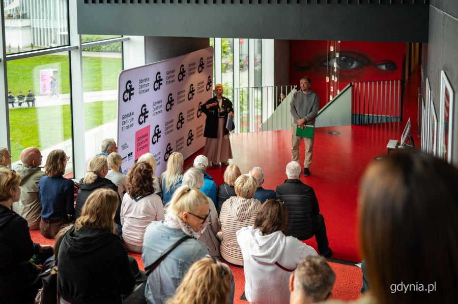 Przewodnicy Danuta Ślipy i Robert Chrzanowski wraz z osobami uczestniczącymi w spacerze Szlakiem Filmowym Gdyni zgromadzeni w Gdyńskim Centrum Filmowym 