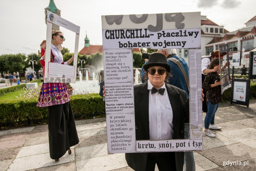 Happening uliczny w ramach Festynu tolerancji. Osoba w czarnym garniturze i białej koszuli trzyma ramkę z wycinkami prasowymi na temat Churchilla // fot. Karol Stańczak