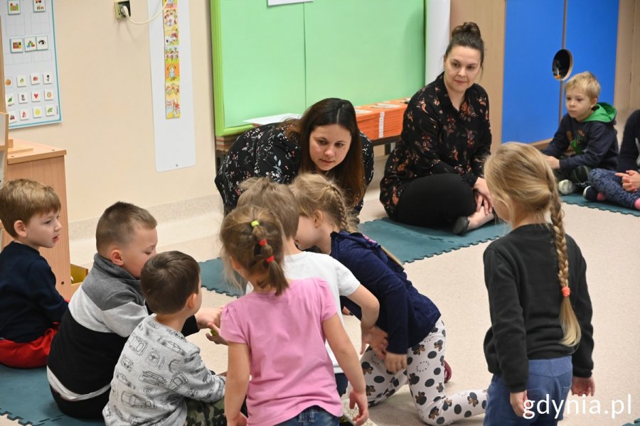 Na zdjęciu znajduje się grupa dzieci, która wraz z nauczycielką wspólnie czyta opowiadanie z serii "ABC Empatii".