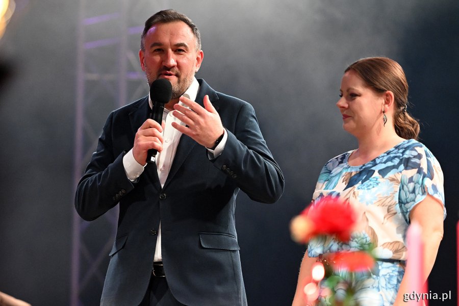 Hala Polsat Plus Arena Gdynia, scena, przemawia Tomasz Augustyniak, trzyma mikrofon, obok stoi Aleksandra Kosiorek
