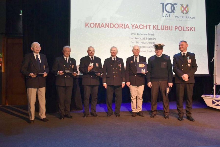 Grupa osób stojąca na scenie i mających za plecami biały ekran