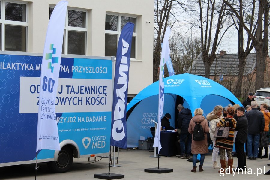 Niebieski bus z napisem "Odkryj tajemnicę zdrowych kości" obok stoi niebieski namiot, oraz kolejka osób