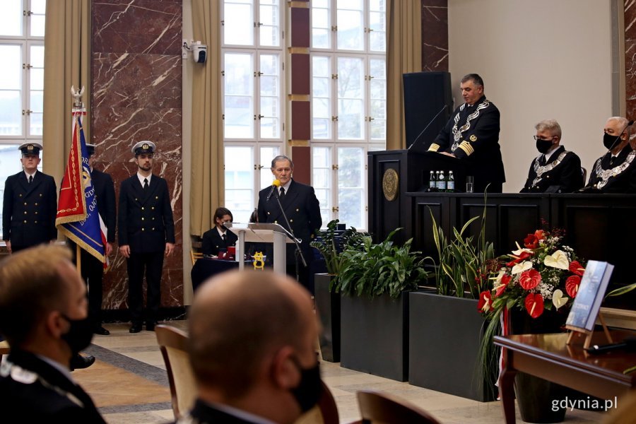 prof. dr hab. inż. kpt. ż. w. Adam Weintrit, rektor Uniwersytetu Morskiego, przemawia podczas uroczystego posiedzenia senatu uczelni (przy górnym podeście). Obok niego inni członkowie senatu uczelni. Poniżej przy mikrofonie - prowadzący uroczystość - Aleksander Gosk oraz poczet sztandarowy ze sztandarem UMG // fot. Przemysław Kozłowski