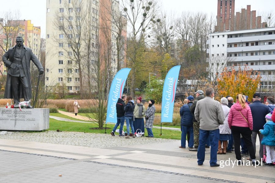 Grupa ludzi stojąca w kolejce na placu przed pomnikiem Józefa Piłsudskiego