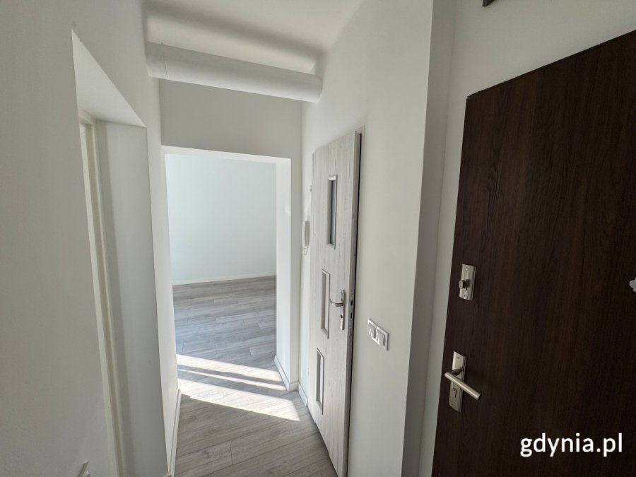 Na zdjęciu widać przedpokój mieszkania komunalnego. W tle widzimy salon mieszkania, na pierwszym planie drzwi wejściowe.