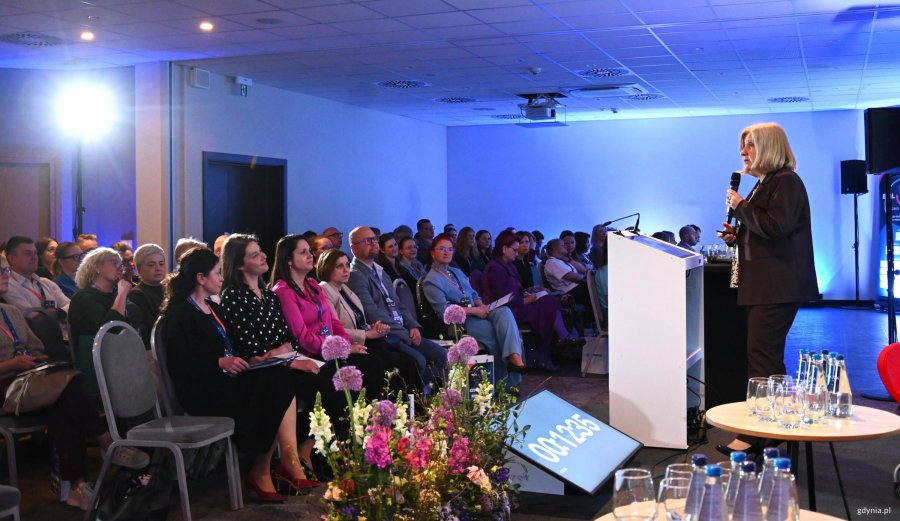 Kobieta na m&oacute;winicy, przed nią tłumy ludzi