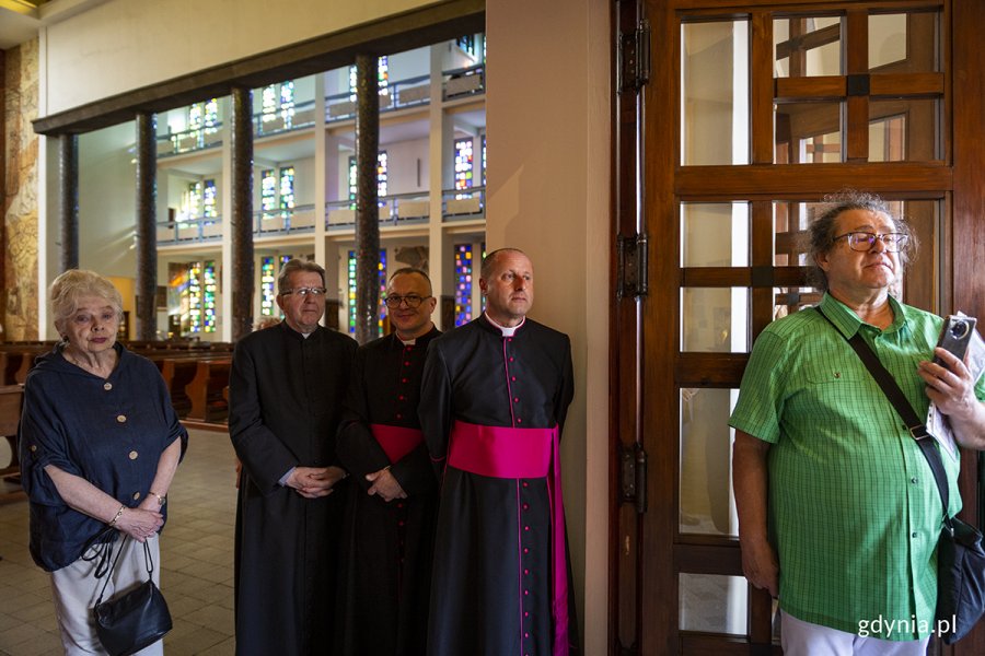 Kilka osób stoi w kościele, wśród nich trzech księży.