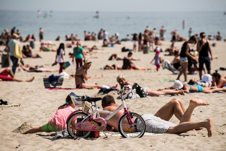 Ludzie wypoczywający na plaży, na pierwszym planie stoi dziecięcy rower. W tle morze. 
