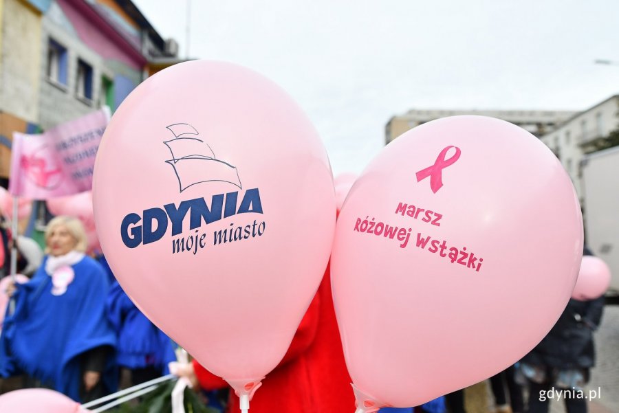 Różowe balony z logotypami Gdyni i Marszu Różowej Wstążki na tle nieba i budynków
