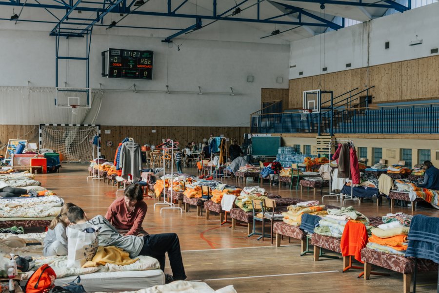 Dzieci na sali gimnastycznej z łóżkami przygotowanymi dla uchodźców