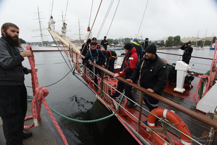 Podchorążowie z Kuwejtu i Kataru, wraz z załogą żaglowca STS „Pogoria” i kadrą uczelnianą wypływają na praktyki morskie. Na dziobie żaglowca stoją studenci. Jedna z osób na brzegu odcumowuje jednostkę // fot. Krzysztof Miłosz/ AMW 