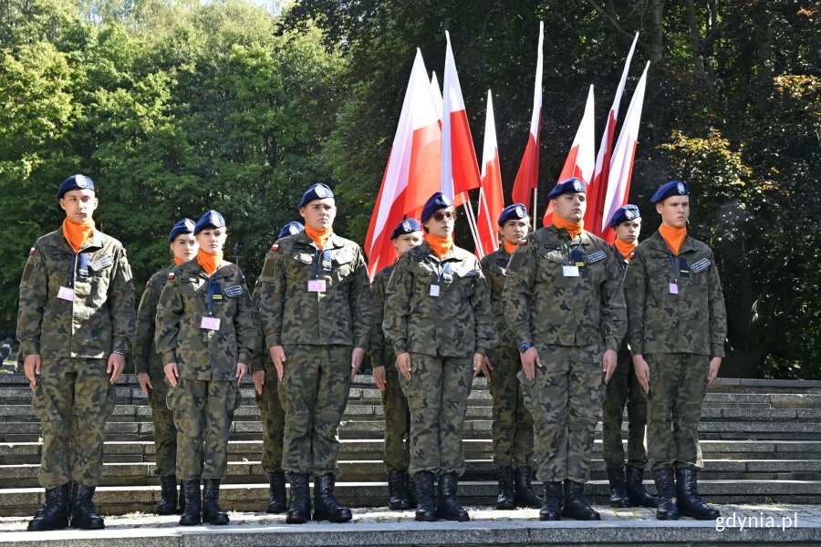 Uczniowie LO w Rzepinie w mundurach stoją w dwuszeregu. W tle biało-czerwone flagi // fot. Magdalena Czernek