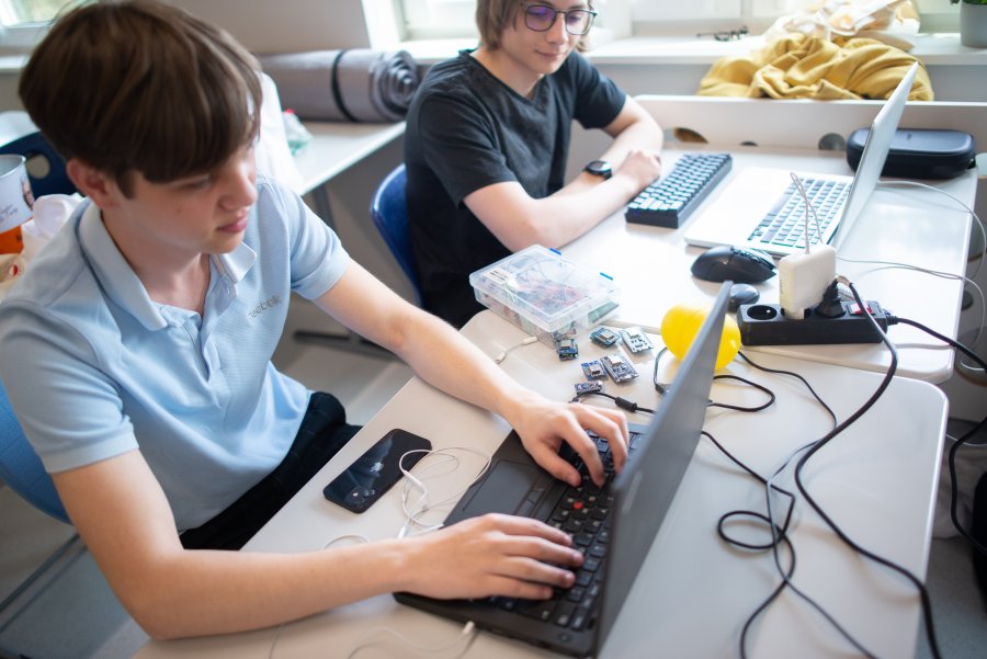 Uczniowie siedzący przy komputerach, pomiędzy nimi specjalne "kostki" elektroniczne