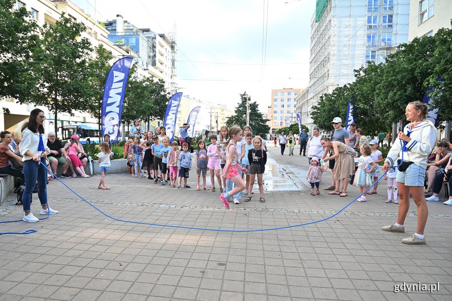 Zabawy dla dzieci na placu Kaszubskim. Dwie animatorki kręca skakanką, przez którą skacze dziewczynka. Grupa dzieci obserwuje zabawę na placu Kaszubskim // fot. Michał Puszczewicz