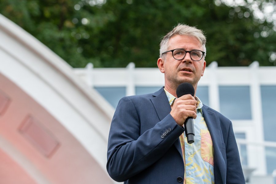 Szymon Kloska - kurator festiwalu "Miasto Słowa" - w ciemnej marynarce i kolorowej koszuli prowadzi spotkanie w Muszli na placu Grunwaldzkim // fot. Anna Rezulak