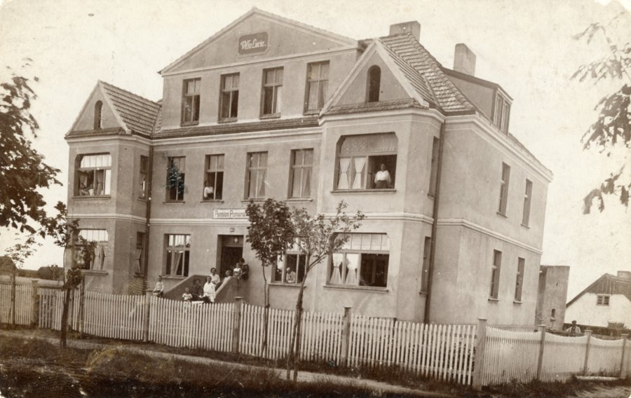 Stara pocztówka Gdyni. Murowany dom, w oknach i na ganku ludzie pozuja do zdjęcia.