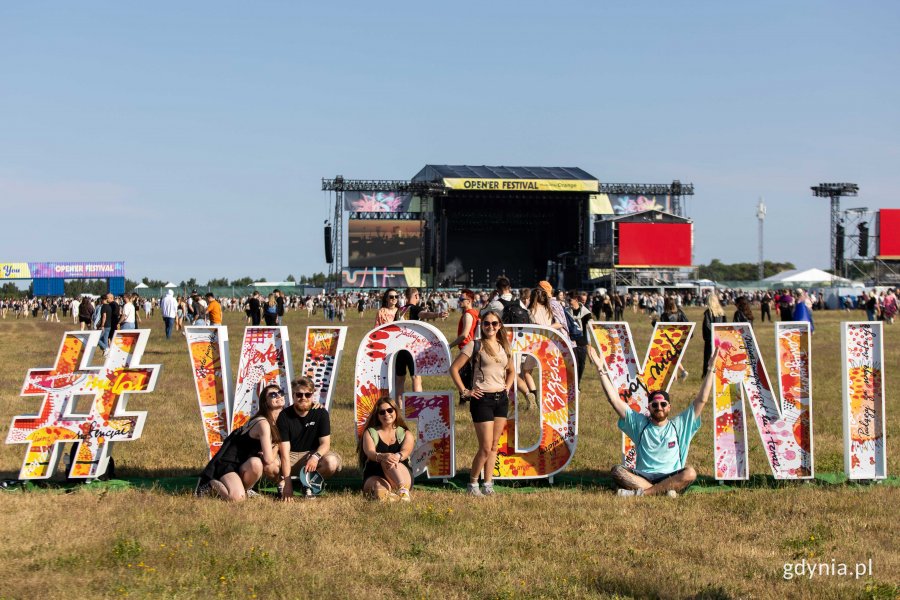 Uczestnicy Open'er Festivalu przy hashtagu #wGdyni, który stoi na terenie festiwalu. W tle: widok na scenę główną // fot. Karol Stańczak