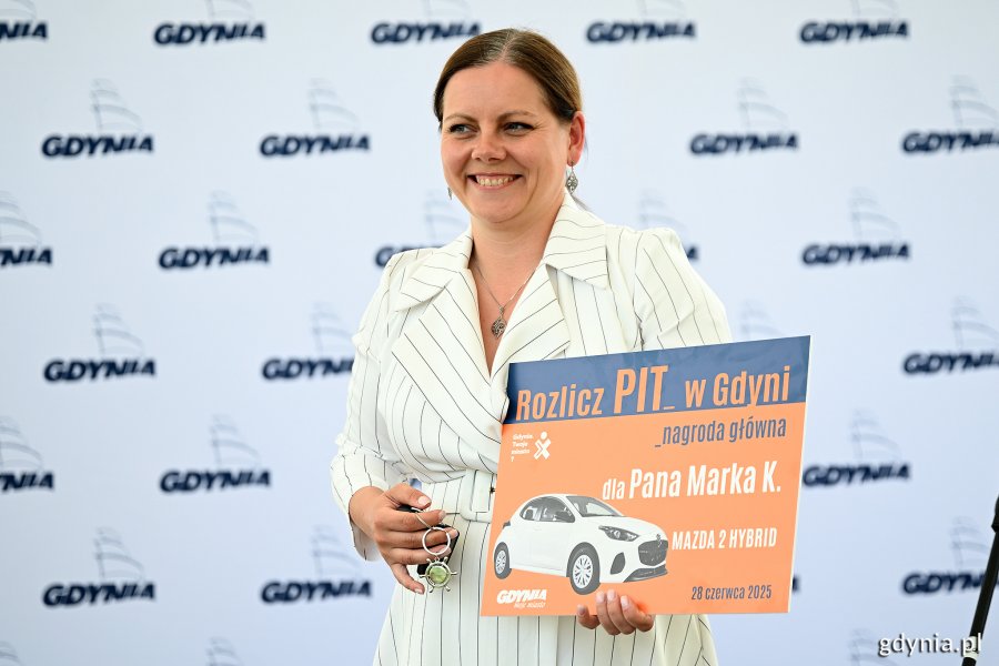 Prezydent Gdyni Aleksandra Kosiorek podczas wręczenia nagród w loterii „Rozlicz PIT w Gdyni” w amfiteatrze na Kamiennej Górze. W ręce trzyma tabliczkę dla jednego ze zwycięzców