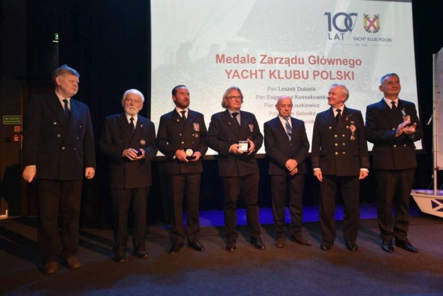 Grupa osób stojących na scenie i mających za plecami biały ekran