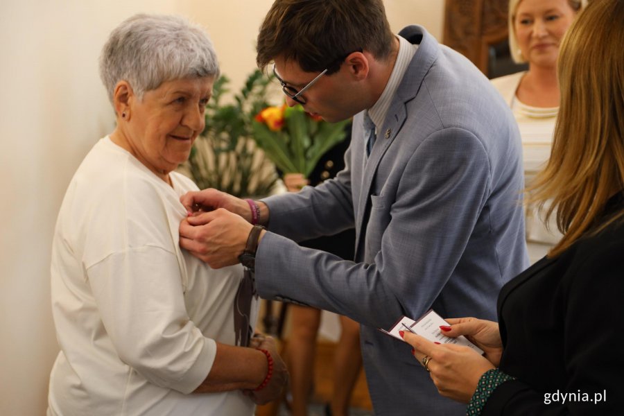 Mężczyzna w garniturze wręcza medal kobiecie białej bluzce