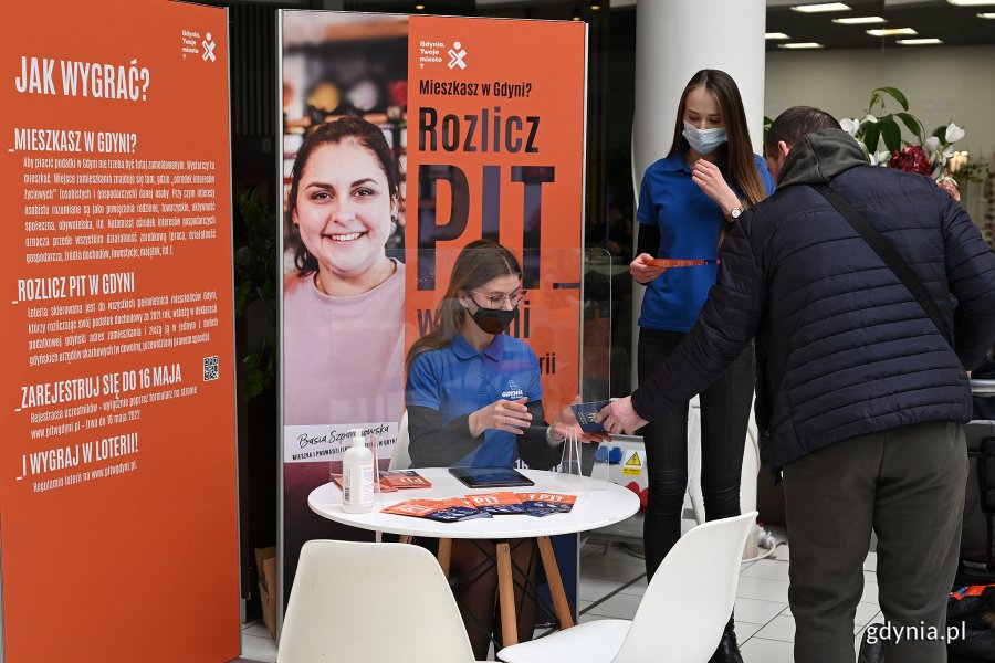 W sobotę, 12 marca konsultacje na temat loterii odbyły się w Galerii Szperk.  Na zdj. dwie konsultantki i mieszkaniec na tle plakatu „Rozlicz PIT w Gdyni” // fot. Michał Puszczewicz