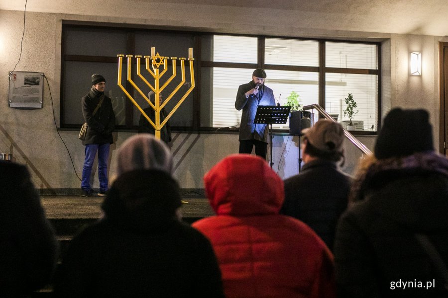 Tomasz Wrosz przemawia przy świeczniku chanukowym przed zgormadzonymi mieszkańcami.