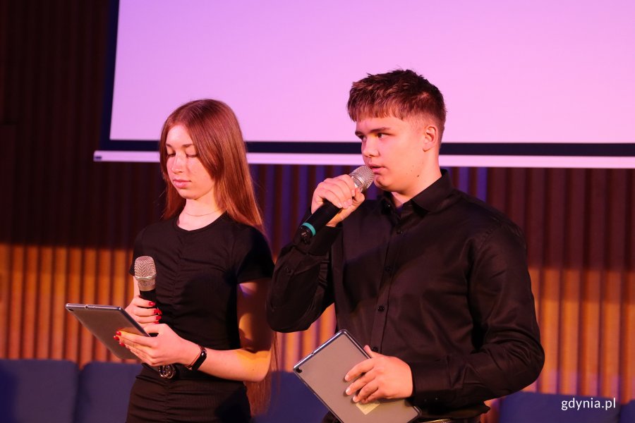 Para młodych ludzi  przemawiajacych przed widownią z mikrofonem w ręku