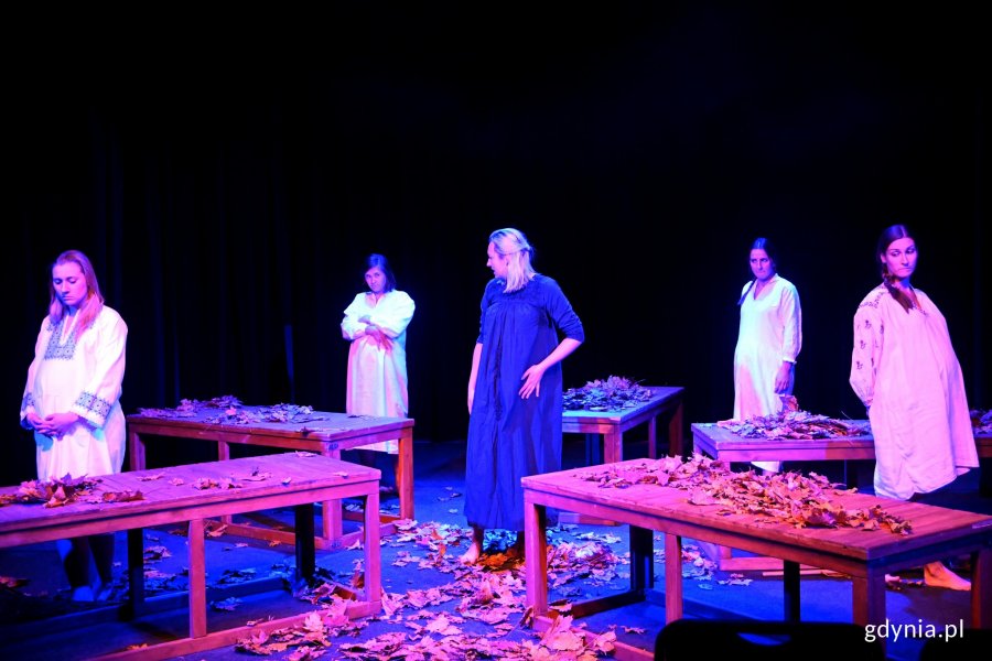 Zdjęcie z próby spektaklu „Skazane kochać” w Konsulacie Kultury. Pięć kobiet ubranych w ludowe ukraińskie stroje, stoją przed drewnianymi stołami, na których są liście // fot. Magdalena Czernek