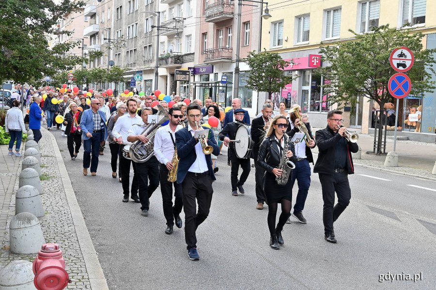 Na czele marszu orkiestra akompaniująca uczestnikom. Na drugim planie uczestnicy przemarszu w ramach V Pomorskiego Dnia Seniora idący ul. Świętojańską