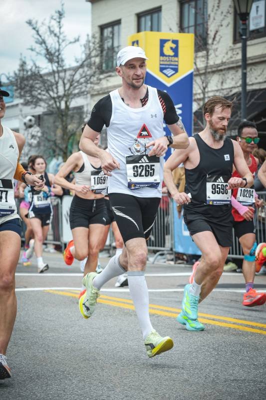 Mężczyzna w czarno-białym stroju sportowym biegnący po ulicach miasta w otoczeniu innych biegaczy