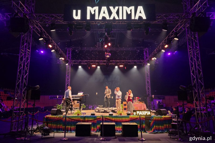 Hala Polsat Plus Arena Gdynia, scena, światła na scenę, aktorzy i muzycy występują, nad sceną wyświetlacz z napisem "U Maxima"