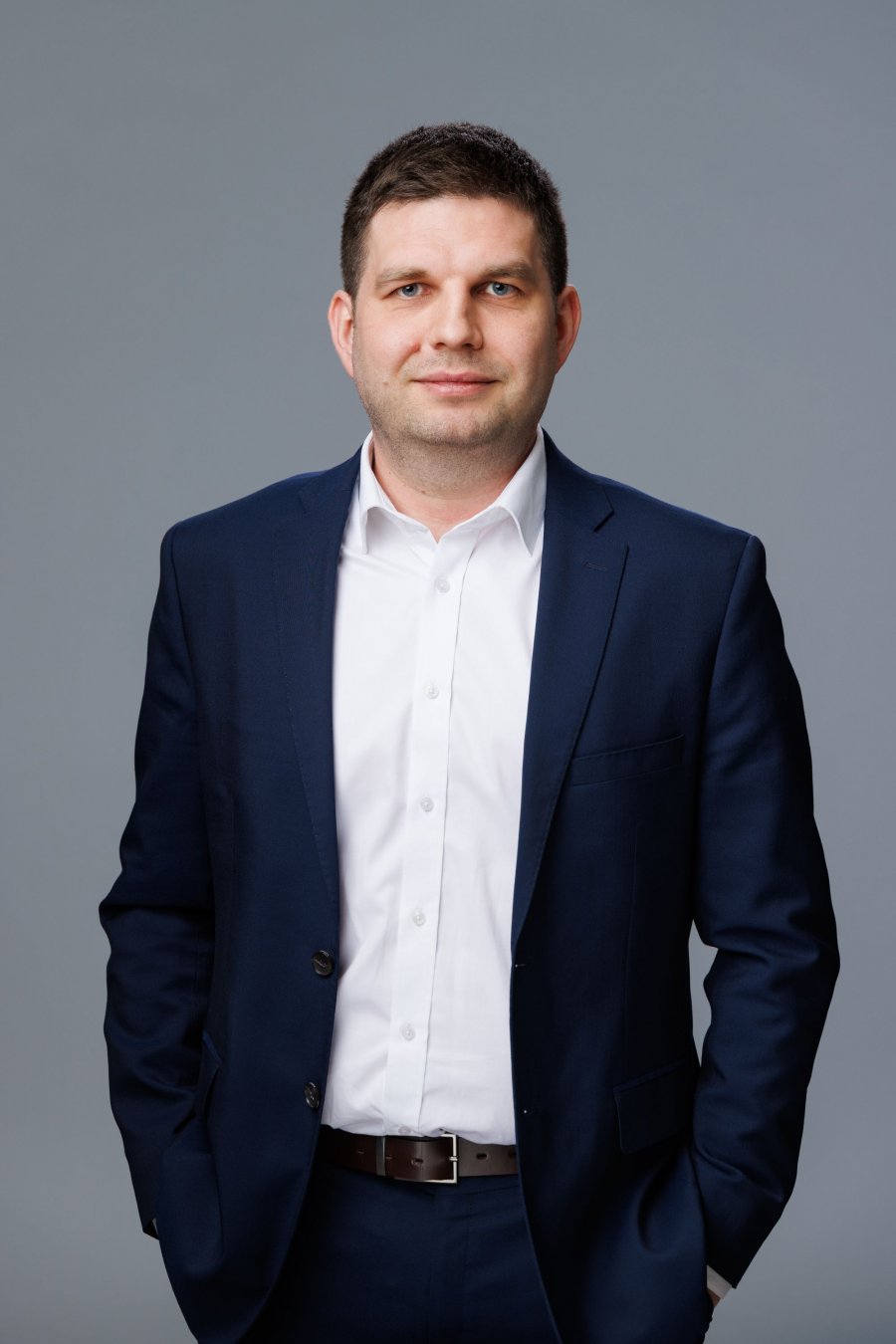 Zdjęcie portertowe: Maciej Zielonka, Wiceprezydent Miasta Gdyni, w garniturze i białej koszuli, na szarym tle. 