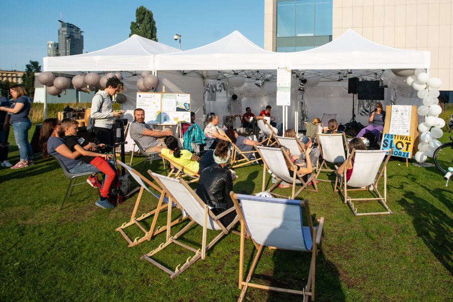 Uczestnicy festiwalu SLOT Pomorze siedzą na leżakach rozstawionych na trawie na placu Grunwaldzkim i słuchają opowieści jeden z prelegentek, która siedzi w białym namiocie // fot. Anna Rezulak