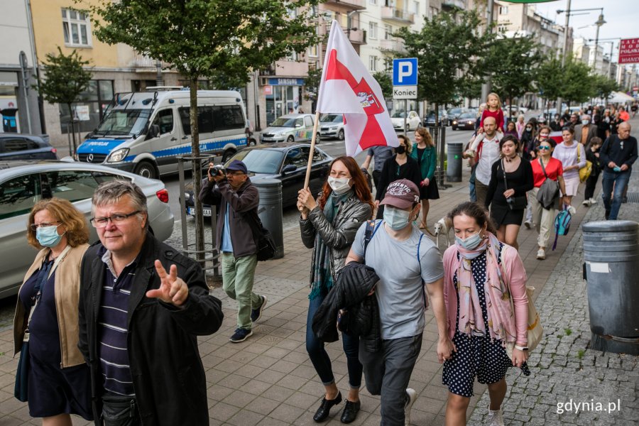 Uczestnicy akcji "Stop przemocy przeciwko narodowi Białorusi" idą ulicą Świętojańską w Gdyni. Jedna z kobiet niesie w ręku flagę białoruską // fot. Karol Stańczak