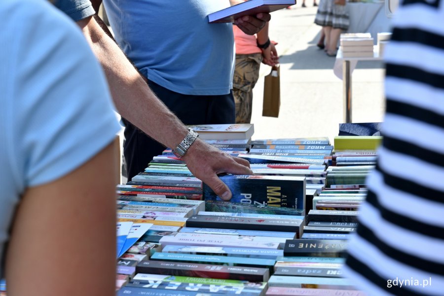 Stół z książkami na Plenerze Literackim w Gdyni. Mężczyzna wyciąga jedną z nich // fot. Magdalena Czernek
