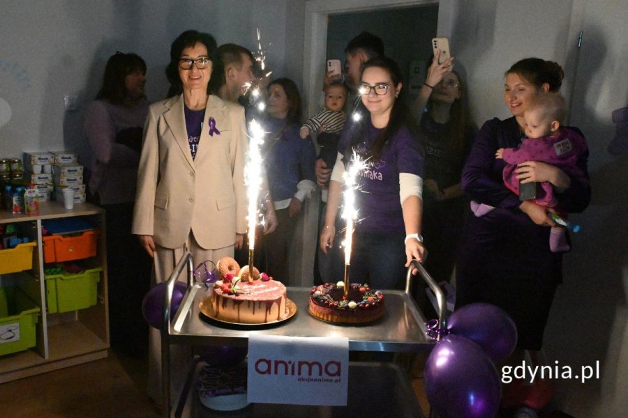 Grupa osób stojąca w ciemnym pomieszczeniu i patrząca na torty z płonącymi świeczkami