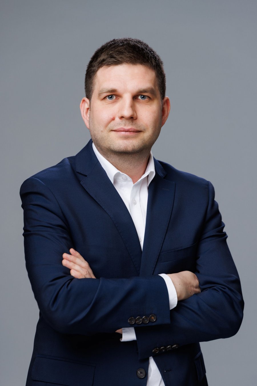 Zdjęcie portertowe: Maciej Zielonka, Wiceprezydent Miasta Gdyni, w garniturze i białej koszuli, na szarym tle. 